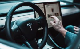 Image of a driver sat behind the wheel of Tesla adjusting the control panel. Tesla have recently announced a recall of most the US models sold